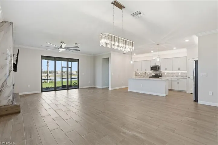 Unfurnished living room featuring a ceiling fan, ornamental molding, wood finish floors, and hanging lights