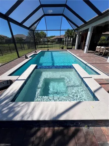 View of swimming pool featuring a pool with connected hot tub, glass enclosure, a sunroom, and a patio