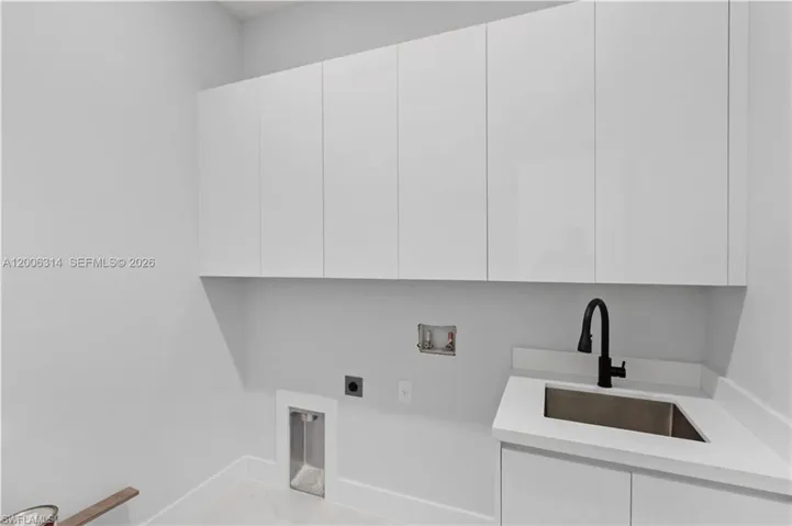 Utility room featuring a built-in sink with a matte black faucet, white upper and lower cabinetry, and a light-toned countertop
