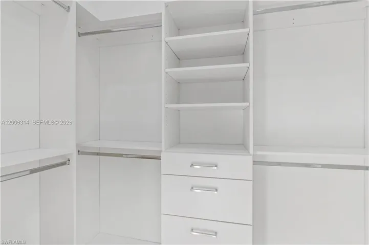 Custom closet system featuring white cabinetry, integrated shelving, three pull-out drawers with chrome hardware, and multiple chrome hanging rods