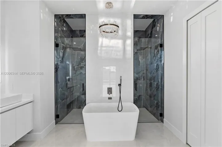 Freestanding soaking tub with a floor-mounted faucet, flanked by two walk-in showers featuring glass enclosures and dark stone-look tile