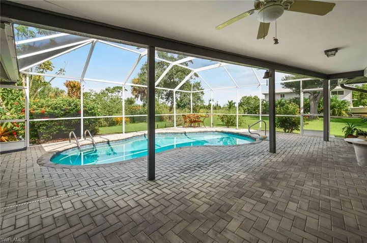 View of pool featuring a patio area, large screened in lanai & lush landscaping views.