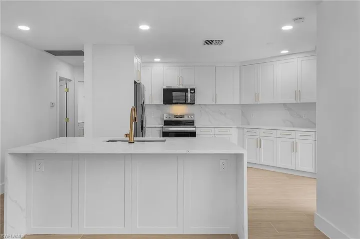 Kitchen featuring an island with sink, white cabinets, and appliances with stainless steel finishes