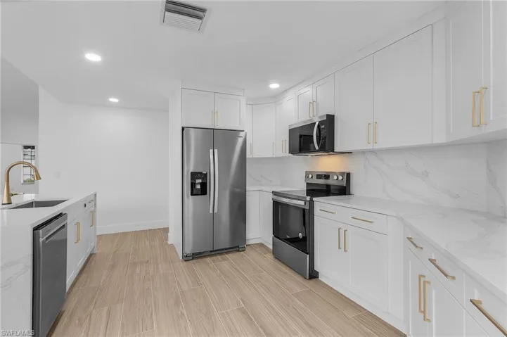 Kitchen with sink, white cabinetry, stainless steel appliances, light stone counters, and tasteful backsplash