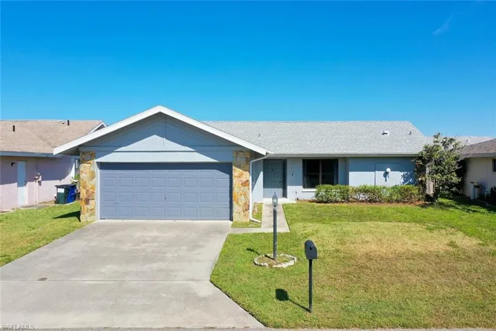 Single story home with a garage, a front yard, stone siding, and driveway