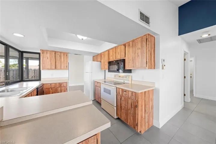 Kitchen with sink, tile patterned floors, black appliances, and a raised ceiling