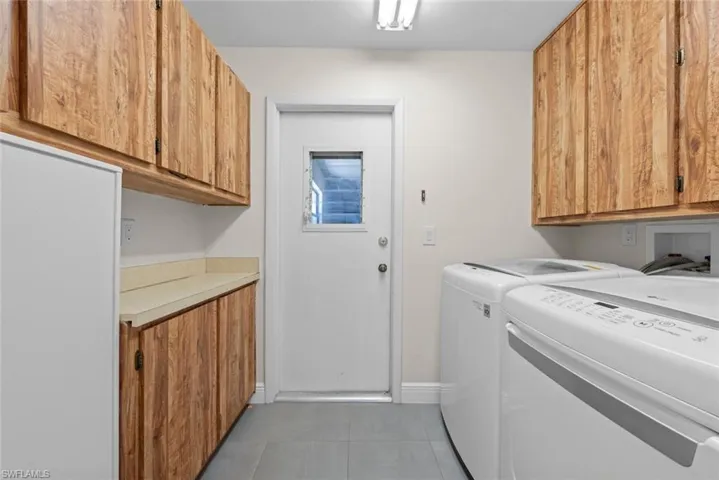 Laundry room featuring cabinet space, light tile patterned floors, baseboards, and separate washer and dryer