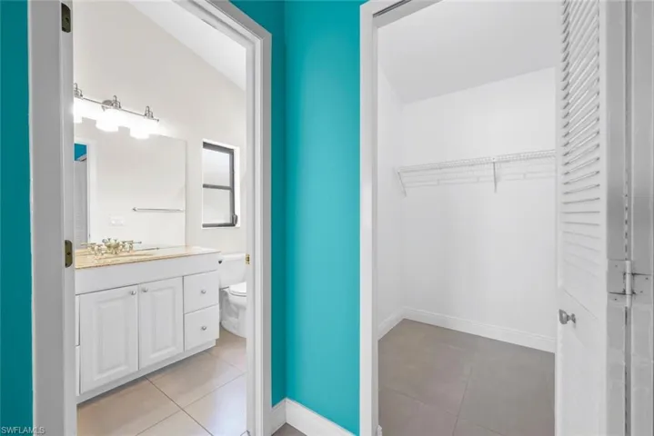 Bathroom featuring baseboards, toilet, tile patterned floors, a walk in closet, and vanity