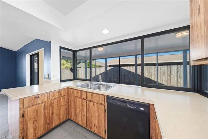 Kitchen featuring light tile patterned floors, sink, black dishwasher, and kitchen peninsula