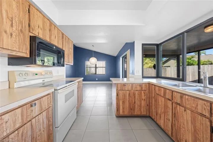 Kitchen with electric stove, sink, vaulted ceiling, light tile patterned flooring, and pendant lighting