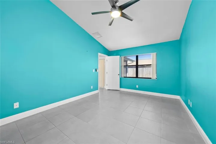 Empty room featuring light tile patterned floors, lofted ceiling, visible vents, ceiling fan, and baseboards