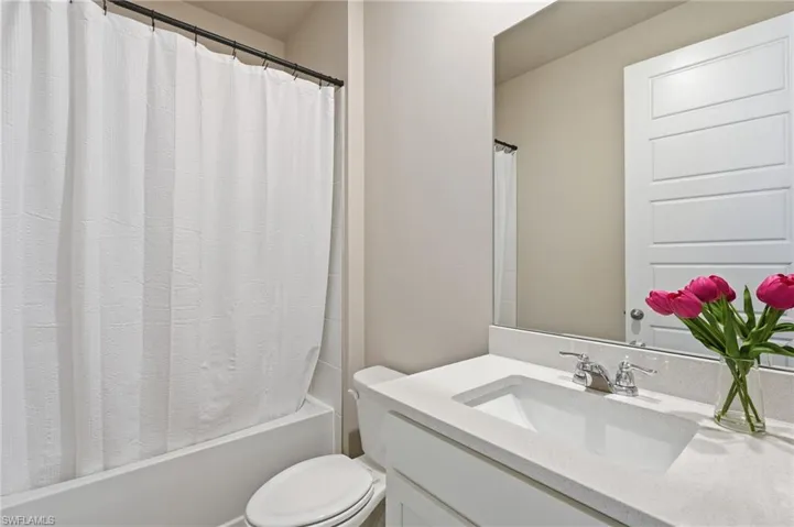 Bathroom featuring a bathtub with shower, toilet, vanity with integrated sink, stone-finish countertop, and wall-mounted mirror