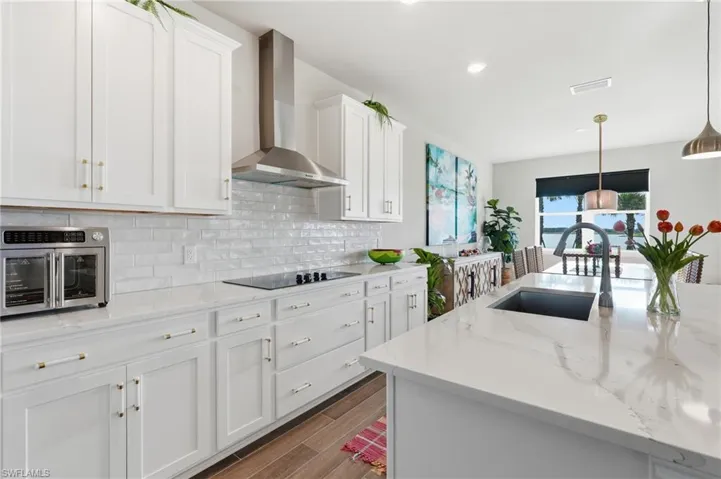 Gourmet kitchen featuring white shaker cabinetry, stainless steel range hood, stone countertops, integrated cooktop, and an undermount sink on the island