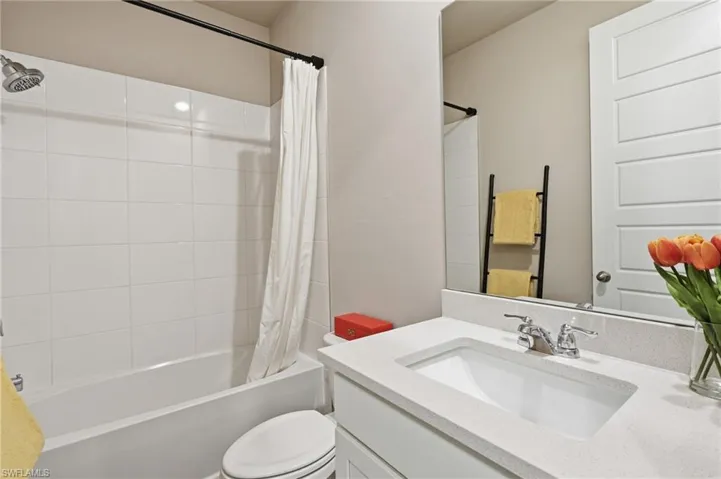 Bathtub with white tile surround, a single vanity with an integrated sink, a chrome faucet, and a large wall-mounted mirror