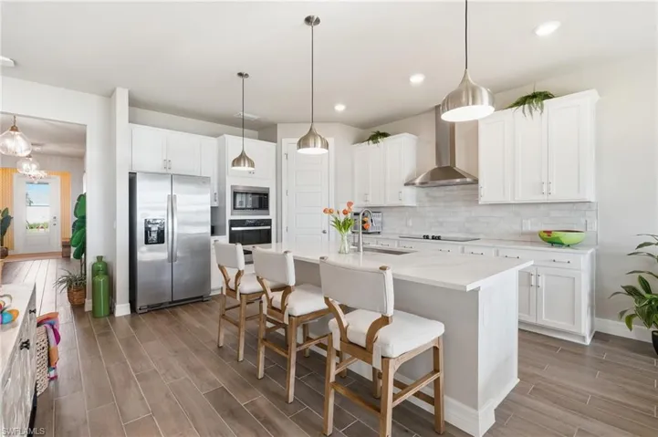 Upgraded kitchen with wall oven & stainless steel appliances, a white island with seating, pendant lighting, and wood-finish flooring