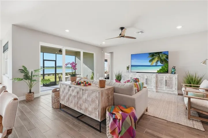 Bright, open-concept living space featuring expansive glass sliding doors with ocean views, wood-finish flooring throughout, a ceiling fan, recessed lighting, and built-in cabinetry