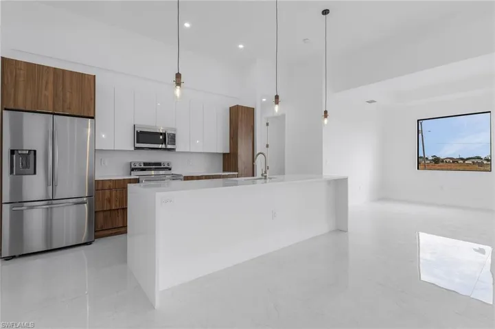Kitchen with appliances with stainless steel finishes, a kitchen island with sink, sink, pendant lighting, and white cabinetry