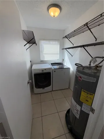 Laundry room with water heater, light tile patterned flooring, a textured ceiling, and washer and clothes dryer