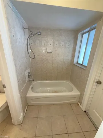 Bathroom with light tile patterned floors and washtub / shower combination