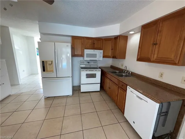 Kitchen featuring wood finish cabinetry, white appliances, light tile patterned floors, a textured ceiling, and ceiling fan