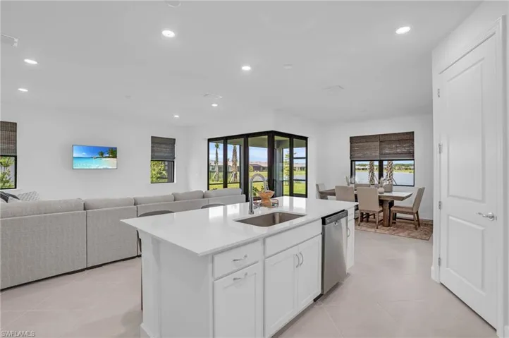 Kitchen featuring white cabinets, sink, light tile patterned floors, stainless steel dishwasher, and an island with sink