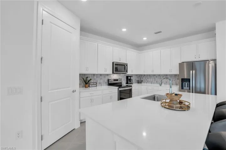 Kitchen featuring light tile patterned flooring, white cabinetry, appliances with stainless steel finishes, decorative backsplash, and sink