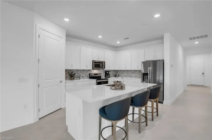 Kitchen featuring sink, stainless steel appliances, a center island with sink, and white cabinets