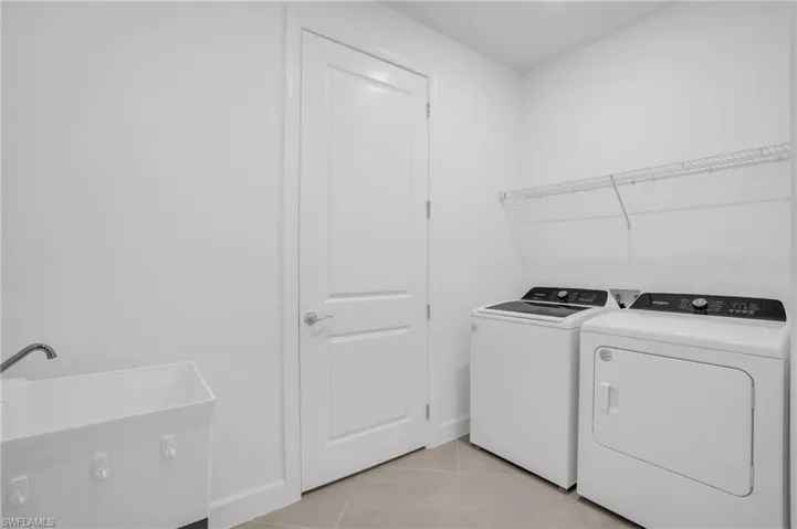 Washroom with washing machine and clothes dryer and light tile patterned floors