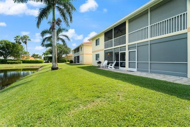 View of green lawn featuring a ceiling fan, a water view, and a balcony