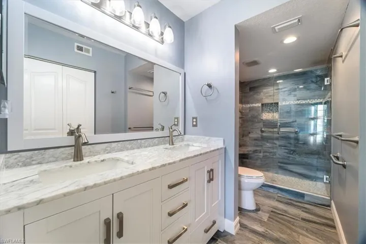 Bathroom with double vanity, a stall shower, wood finished floors, and recessed lighting