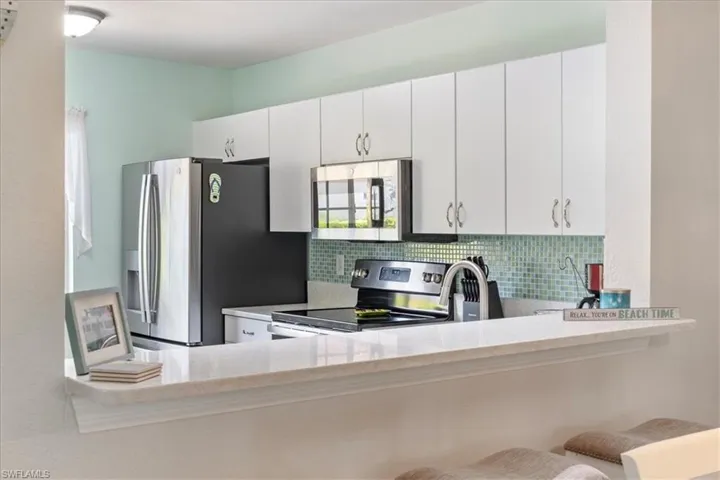 Kitchen with appliances with stainless steel finishes, tasteful backsplash, white cabinetry, and light stone countertops