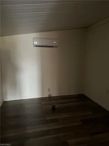 Empty room featuring dark wood-type flooring, lofted ceiling, and a wall unit AC