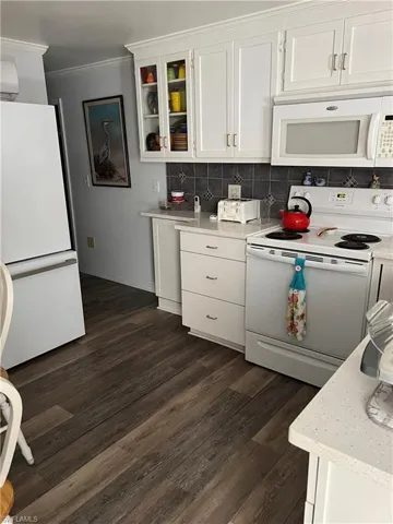 Kitchen featuring tasteful backsplash, white cabinetry, dark hardwood / wood-style floors, crown molding, and white appliances