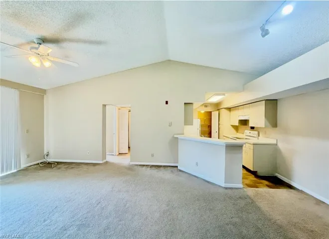 Unfurnished living room with baseboards, carpet flooring, ceiling fan, and vaulted ceiling