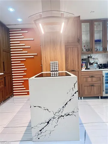 Kitchen with beverage cooler, stainless steel gas stovetop, glass insert cabinets, light tile patterned flooring, and brown cabinetry