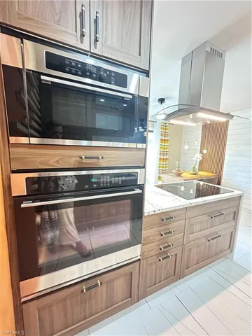Kitchen with cooktop, double oven, extractor fan, and light stone counters