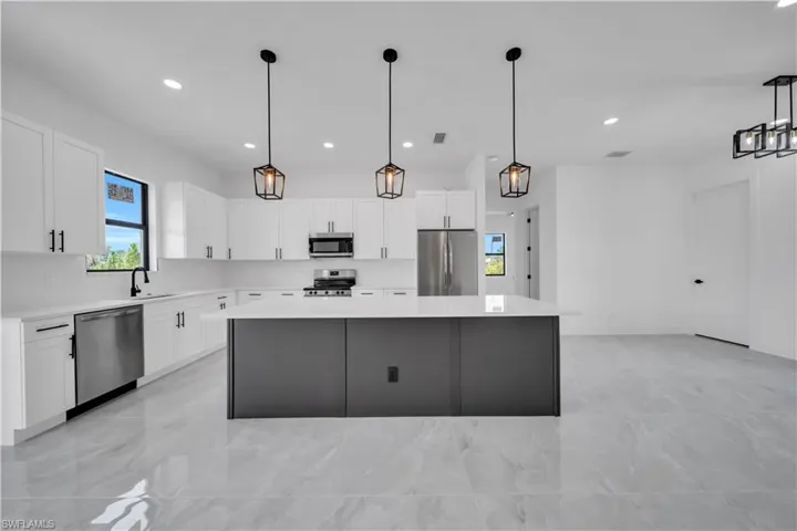 Kitchen featuring appliances with stainless steel finishes, light marble finish flooring, a center island, light countertops, and white cabinetry
