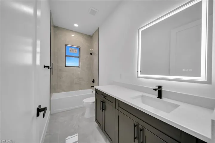 Bathroom with vanity, shower / bathtub combination, marble finish flooring, and recessed lighting