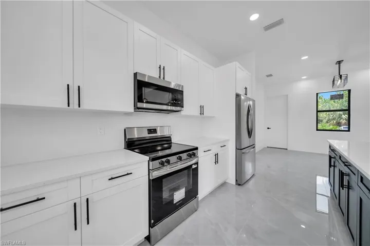 Kitchen with appliances with stainless steel finishes, white cabinetry, recessed lighting, light stone counters, and hanging light fixtures