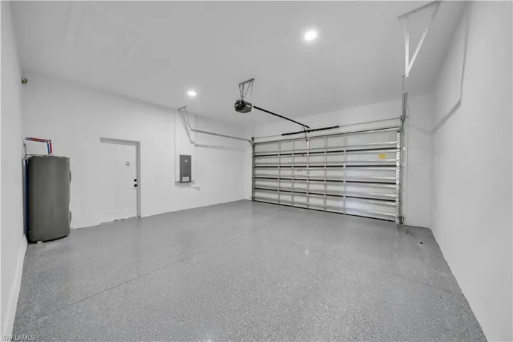 Garage with electric panel, water heater, recessed lighting, and a garage door opener