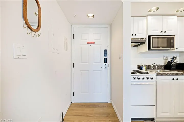 Kitchen featuring stainless steel microwave, white range, white cabinetry, light wood-style flooring, and dark countertops