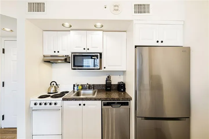 Kitchen featuring appliances with stainless steel finishes, under cabinet range hood, dark countertops, and white cabinets