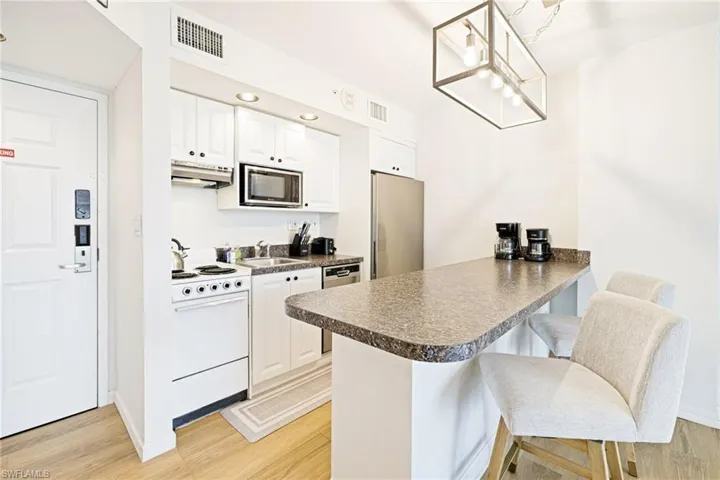 Kitchen with stainless steel appliances, under cabinet range hood, dark countertops, a peninsula, and light wood-style flooring