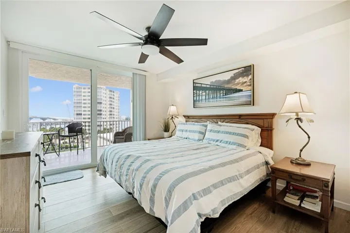 Bedroom with access to exterior, wood finished floors, expansive windows, and a ceiling fan