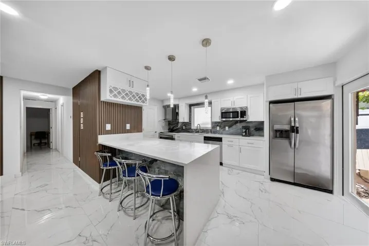Contemporary kitchen featuring an oversized island with a solid surface countertop, white shaker cabinetry, stainless steel appliances, and large format marble-look tile flooring
