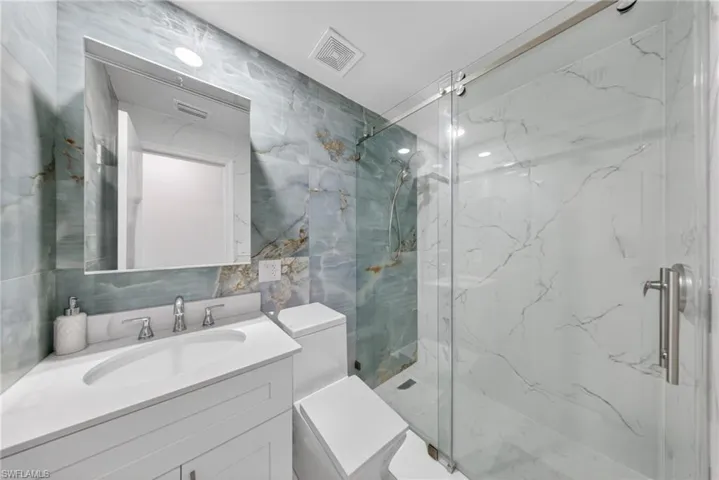 Bathroom featuring a walk-in shower with clear glass enclosure, white vanity with integrated sink, modern chrome faucet, and full-height wall tiling