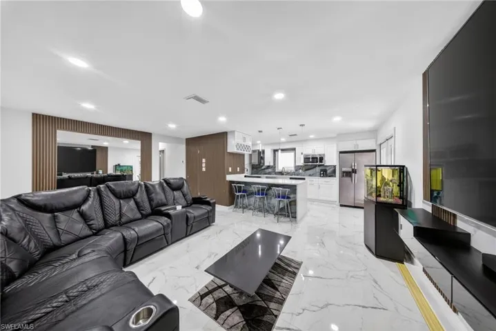 Open-concept living space featuring white marble-look flooring, recessed lighting, and a kitchen island with seating
