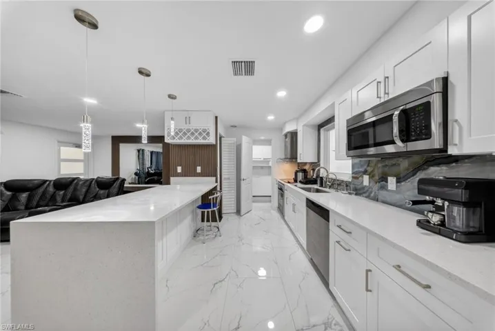 Open-concept kitchen featuring an expansive island with a waterfall edge, white shaker cabinetry, stainless steel appliances, a unique backsplash, and polished porcelain flooring
