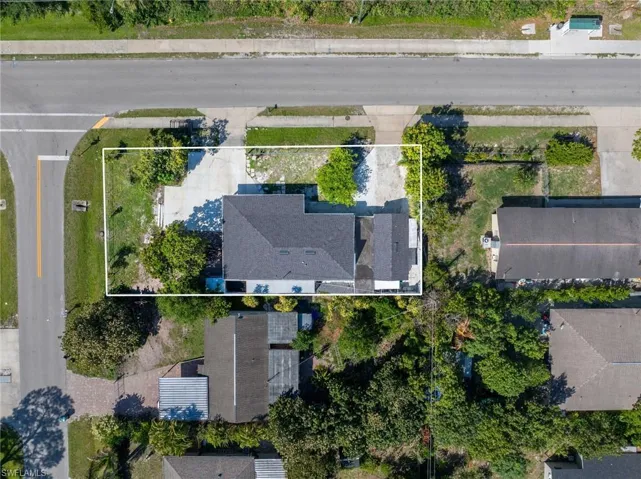 Property featuring a dark shingle roof, a concrete driveway, and surrounding green landscaping