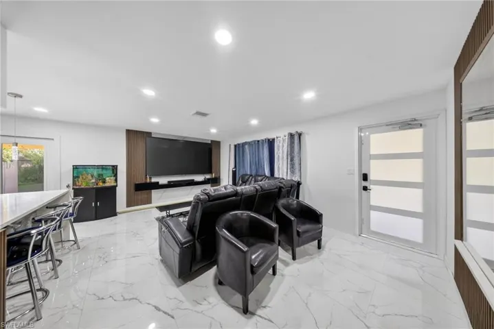 Open-concept living space with large format porcelain tile flooring, recessed lighting, and a contemporary media wall with wood-finish paneling